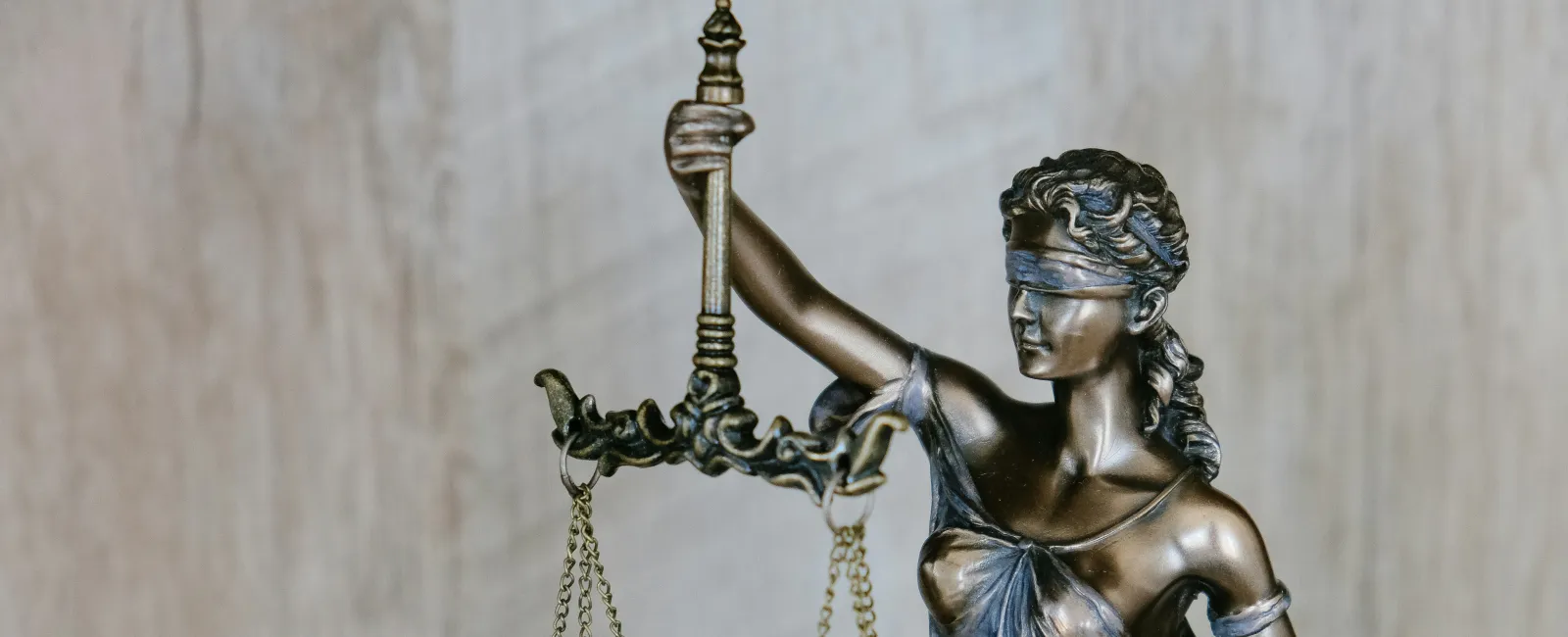 Bronze Lady Justice statue blindfolded holding balanced scales against a neutral background representing a law firm.