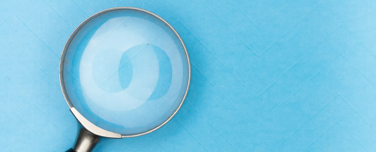 Magnifying glass with black handle on a blue textured background focusing light reflection.