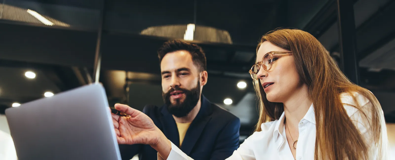 Two professionals collaborating and discussing work on a laptop in a modern office setting.