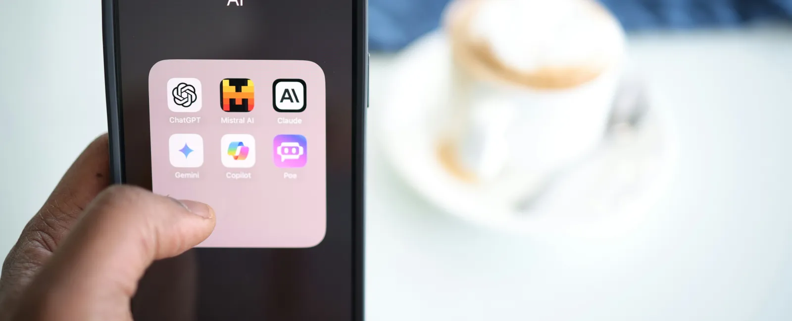 Hand holding smartphone displaying folder with AI app icons like ChatGPT, Mistral AI, and Claude on screen.