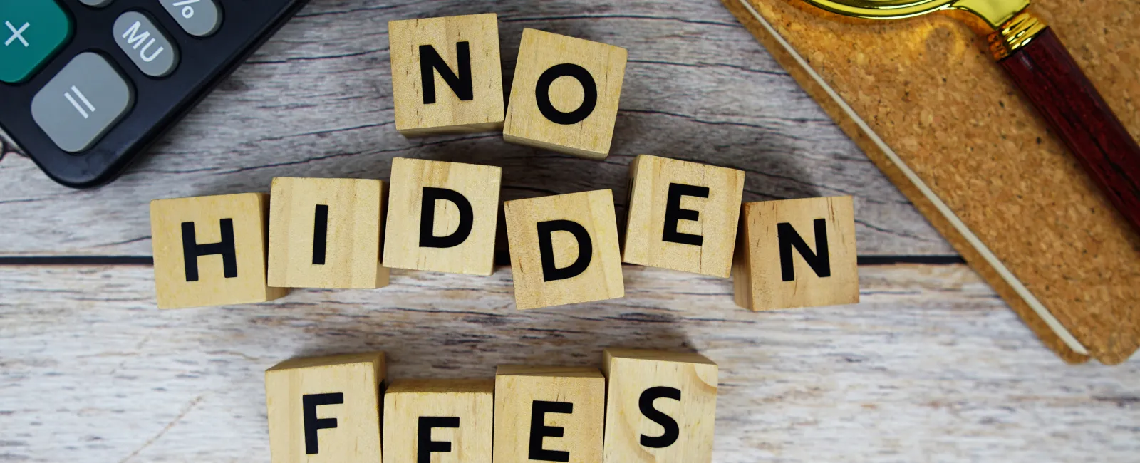 Wooden blocks spelling No Hidden Fees next to calculator, magnifying glass, and notebook on wooden surface.
