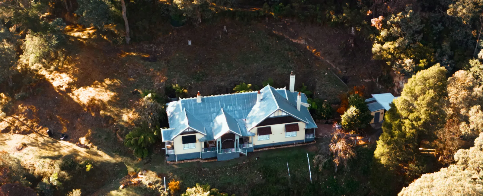 Aerial view of a house surrounded by dense trees and forest in golden sunlight during autumn.