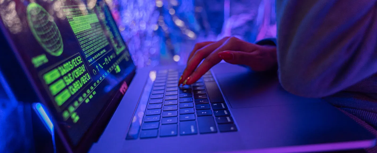 Person typing on laptop with green digital data overlays in a blue and purple ambient light environment.