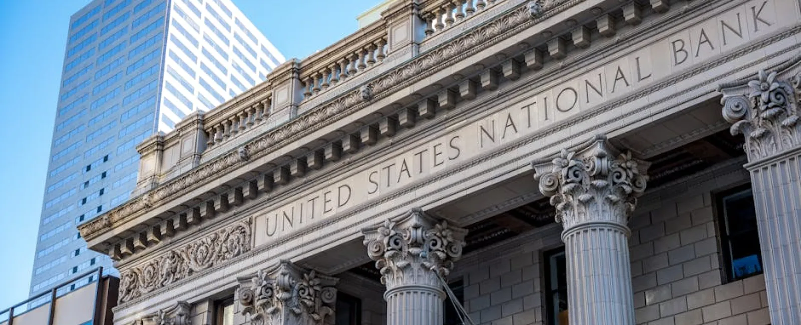 Historic United States National Bank building with Corinthian columns and modern skyscraper in background.