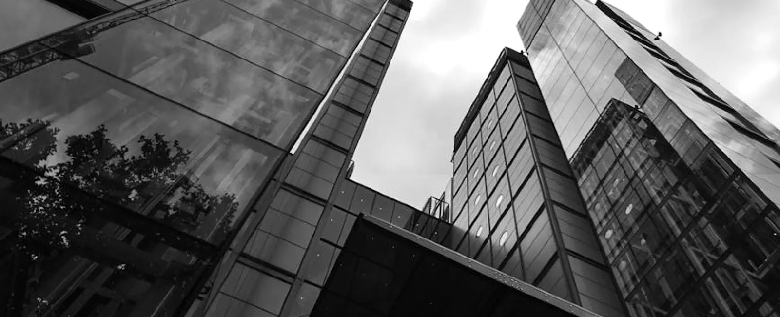 Black and white photo of modern glass skyscrapers viewed from below against a cloudy sky.