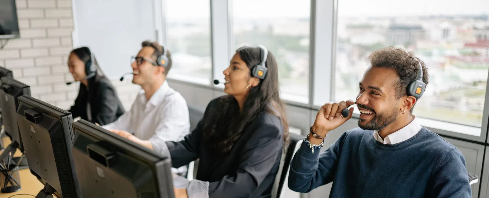 Customer service team wearing headsets working on computers in a bright office with large windows.