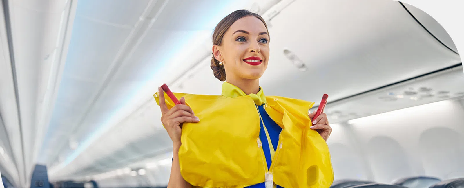 Flight attendant demonstrating the use of a yellow life vest inside an airplane cabin.