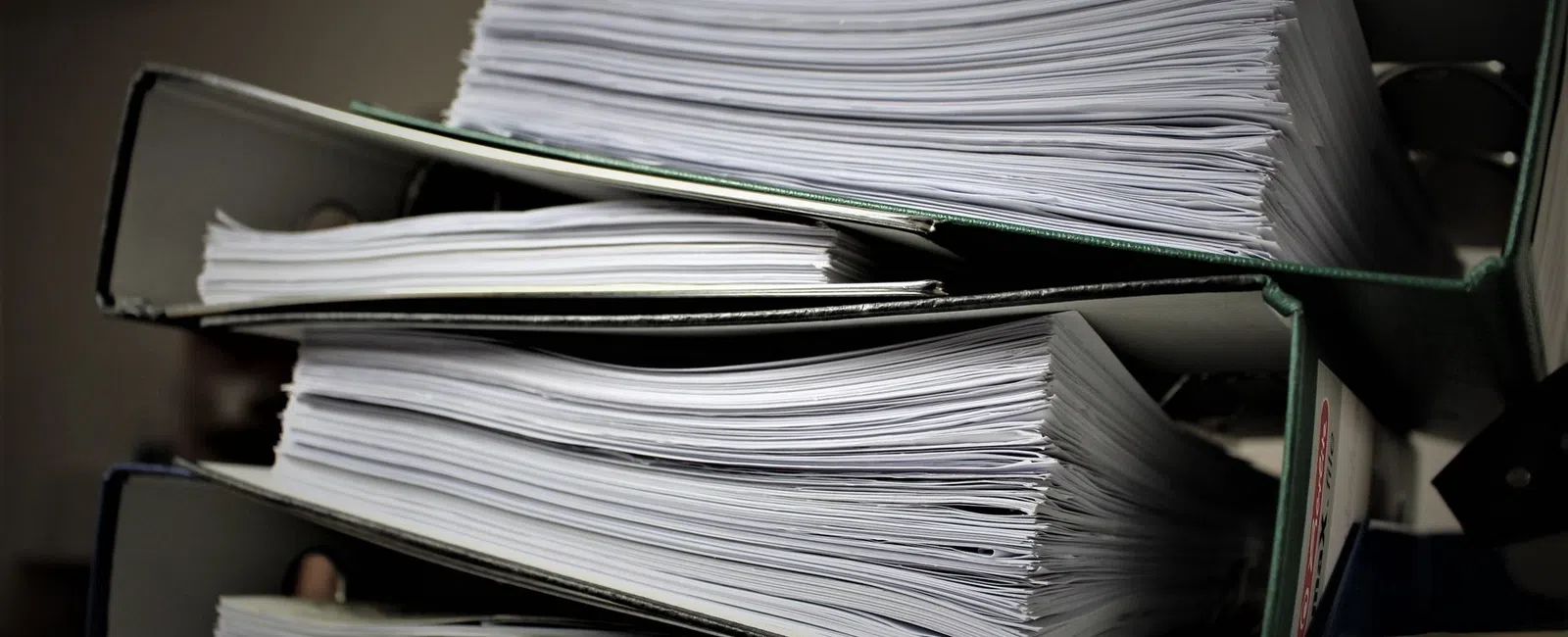 Stack of thick binders filled with numerous white printed documents on a dark background