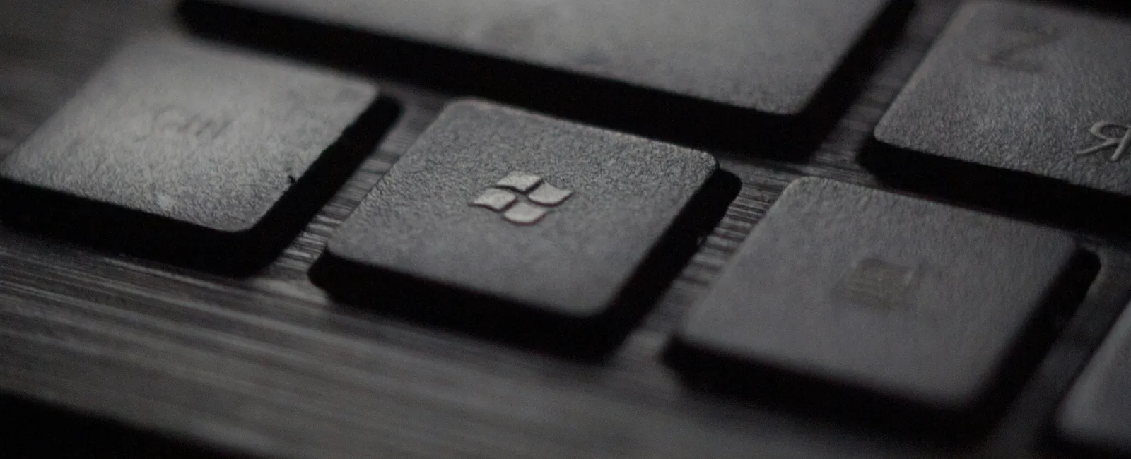 Close-up of black keyboard keys with a Windows logo key in focus on a wooden surface.