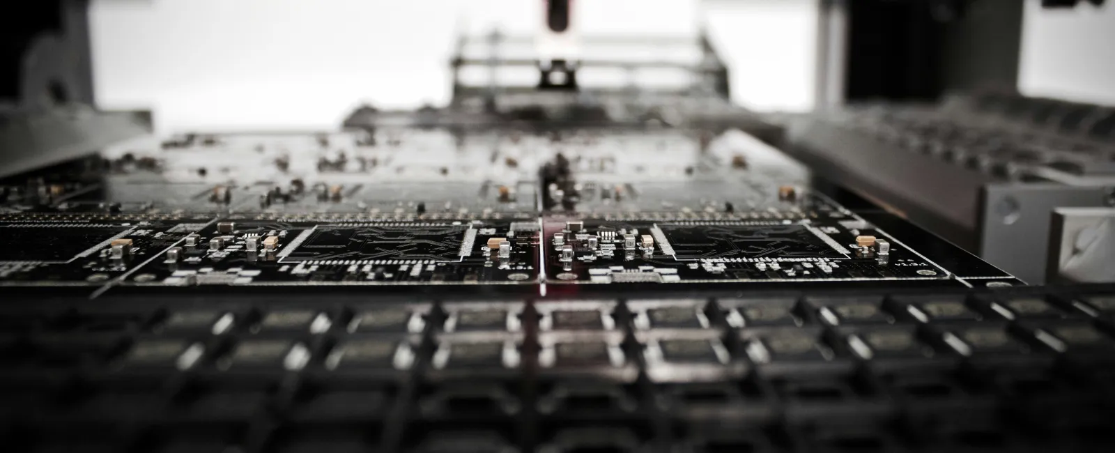 Close-up of a circuit board manufacturing process with a red robotic arm placing components on PCBs.