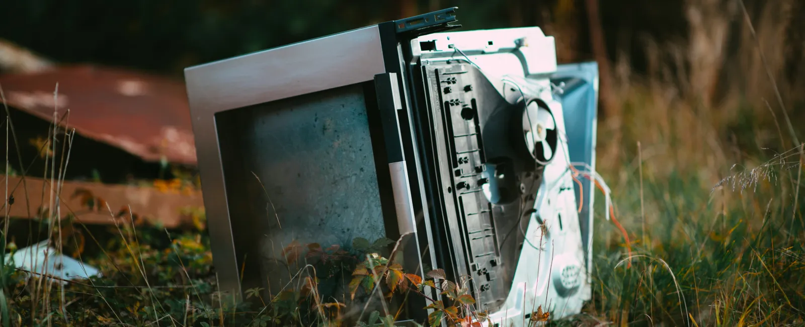 Broken computer lying in tall grass outdoors after a natural disaster.