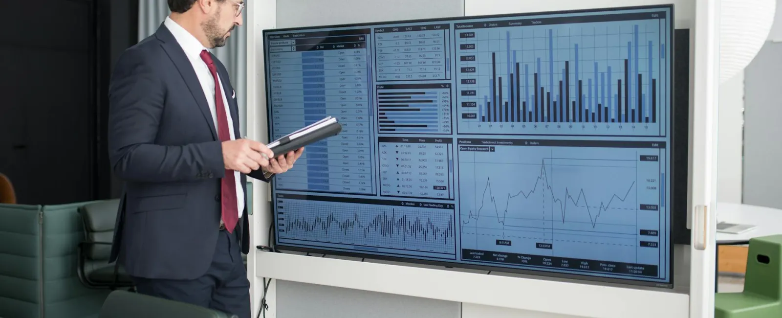 Businessman in suit analyzing financial data and charts on a large screen in modern office conference room.