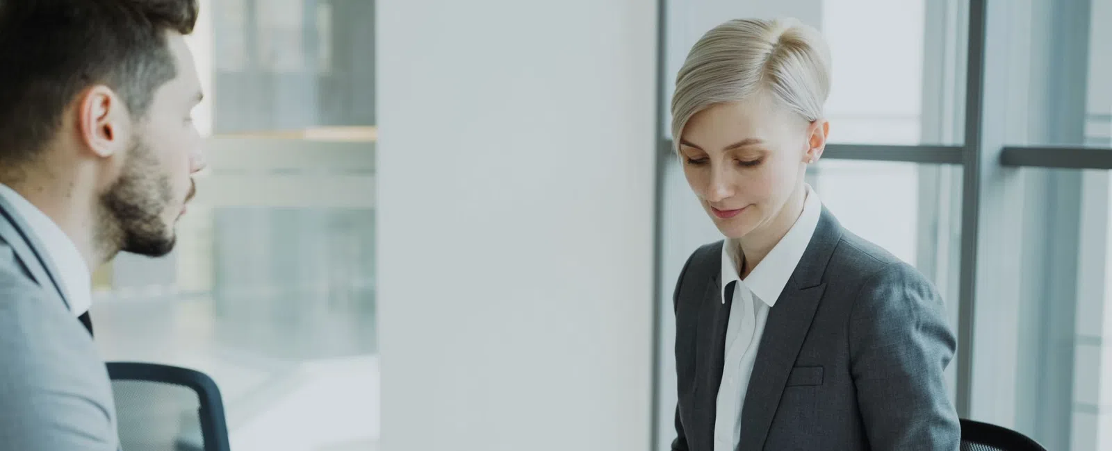 Professional businesswoman reviewing documents on a tablet while interviewing a man in a modern office.