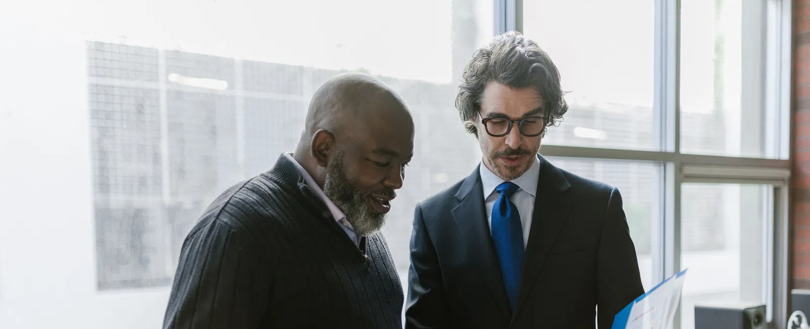 Two businessmen discussing documents in a bright modern office near large windows during a meeting