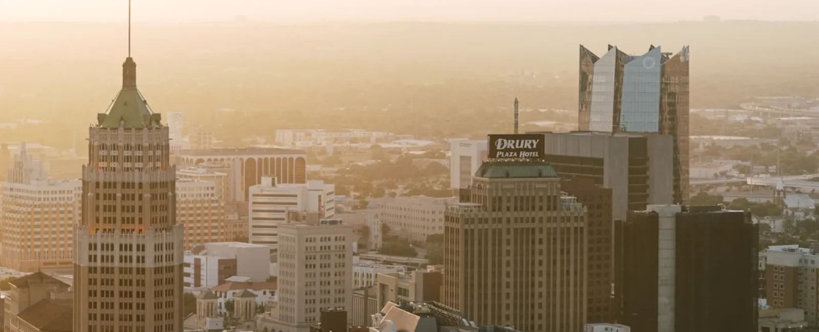 Downtown cityscape at sunrise with tall buildings, including a tower with a waving American flag.