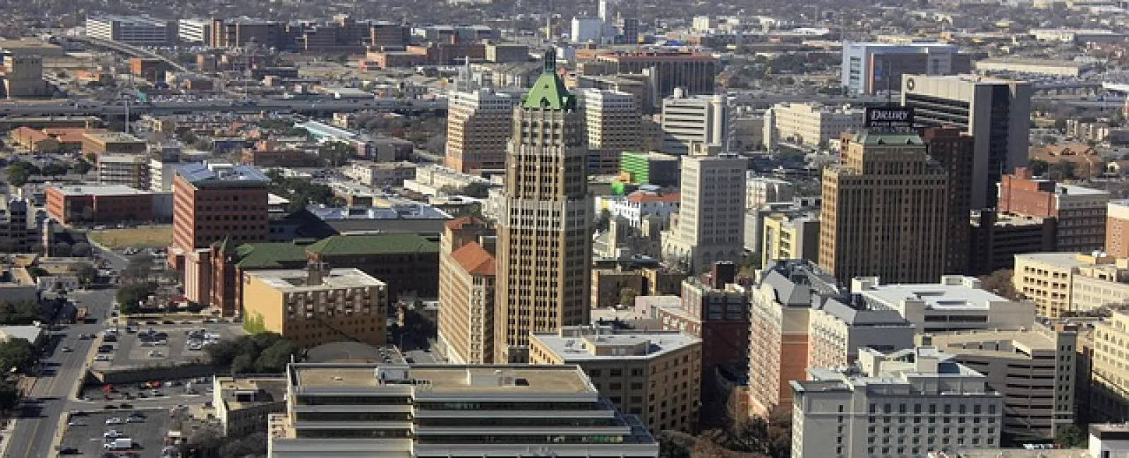 Aerial view of a dense urban cityscape with various commercial and residential buildings under a clear sky.