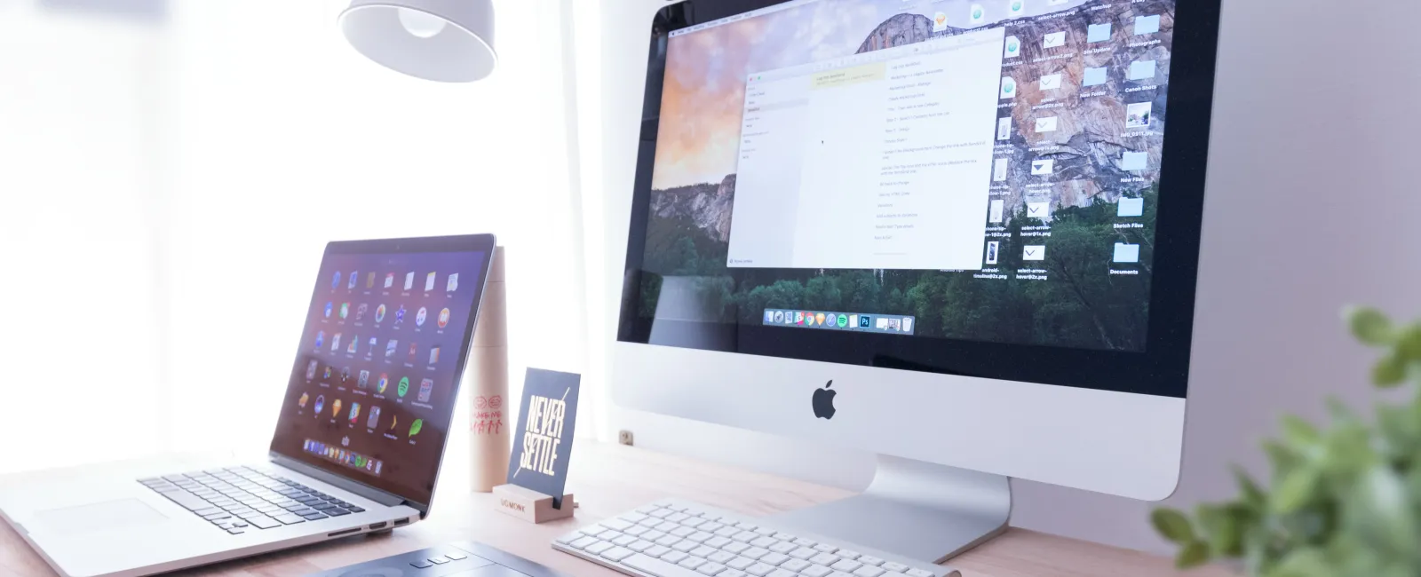 Bright workspace with Apple iMac, MacBook, drawing tablet, iPhone, and desk lamp on wooden desk.