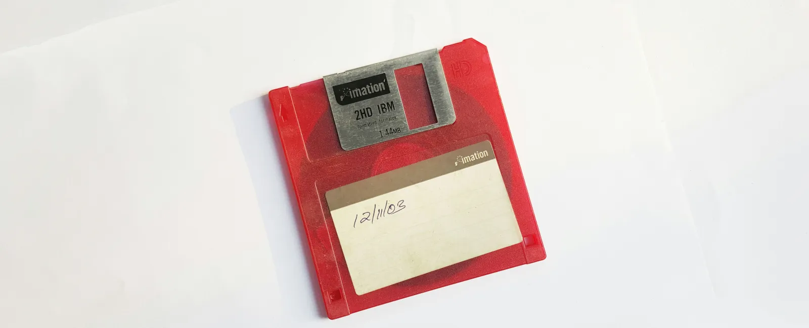 Red 3.5-inch floppy disk with a handwritten date label on a white background showing how outdated tech isnt; helpful