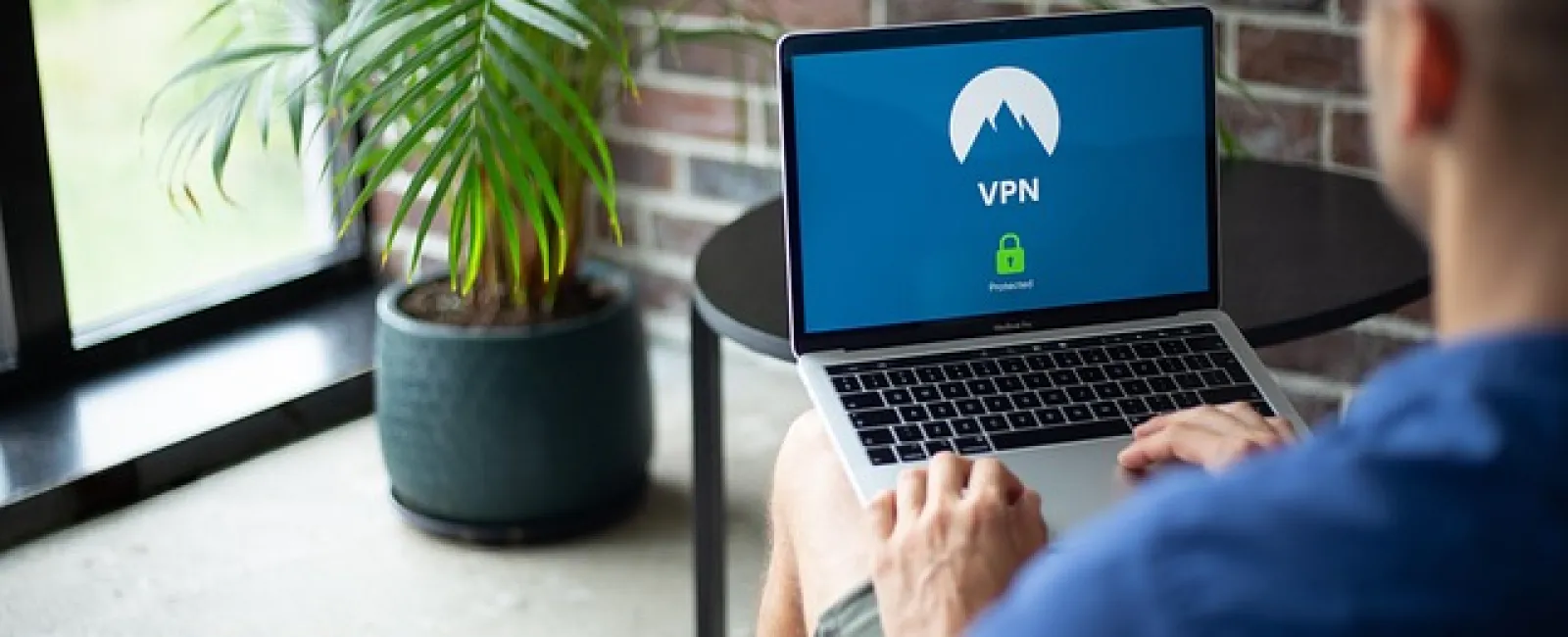 Person using a laptop with a VPN confirmation screen in a cozy room with brick wall and plant.
