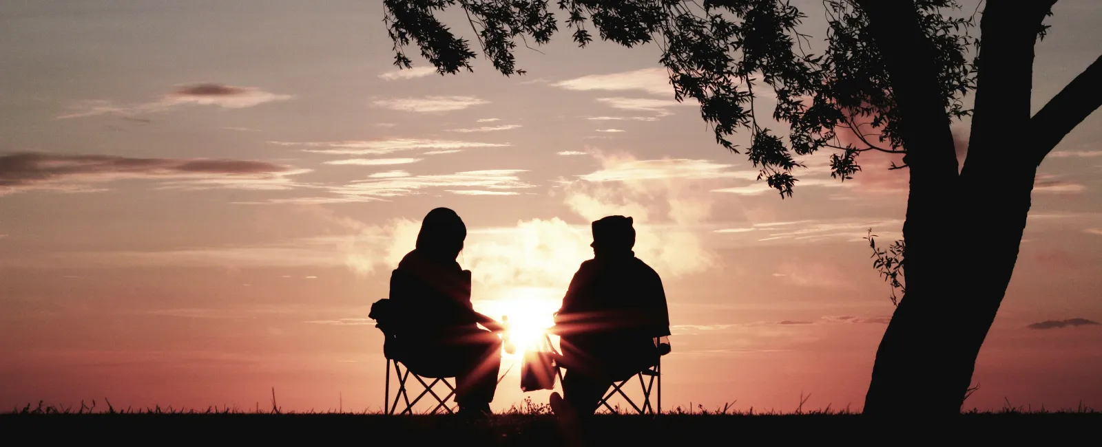 a couple sitting on a bench at sunset