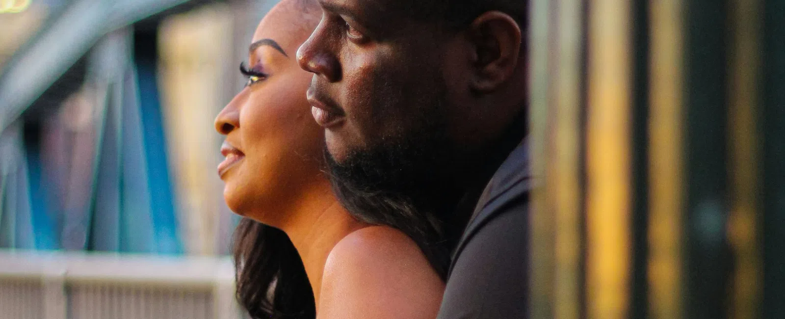 Couple leaning on a railing overlooking an urban scene at sunset, sharing a quiet moment together.
