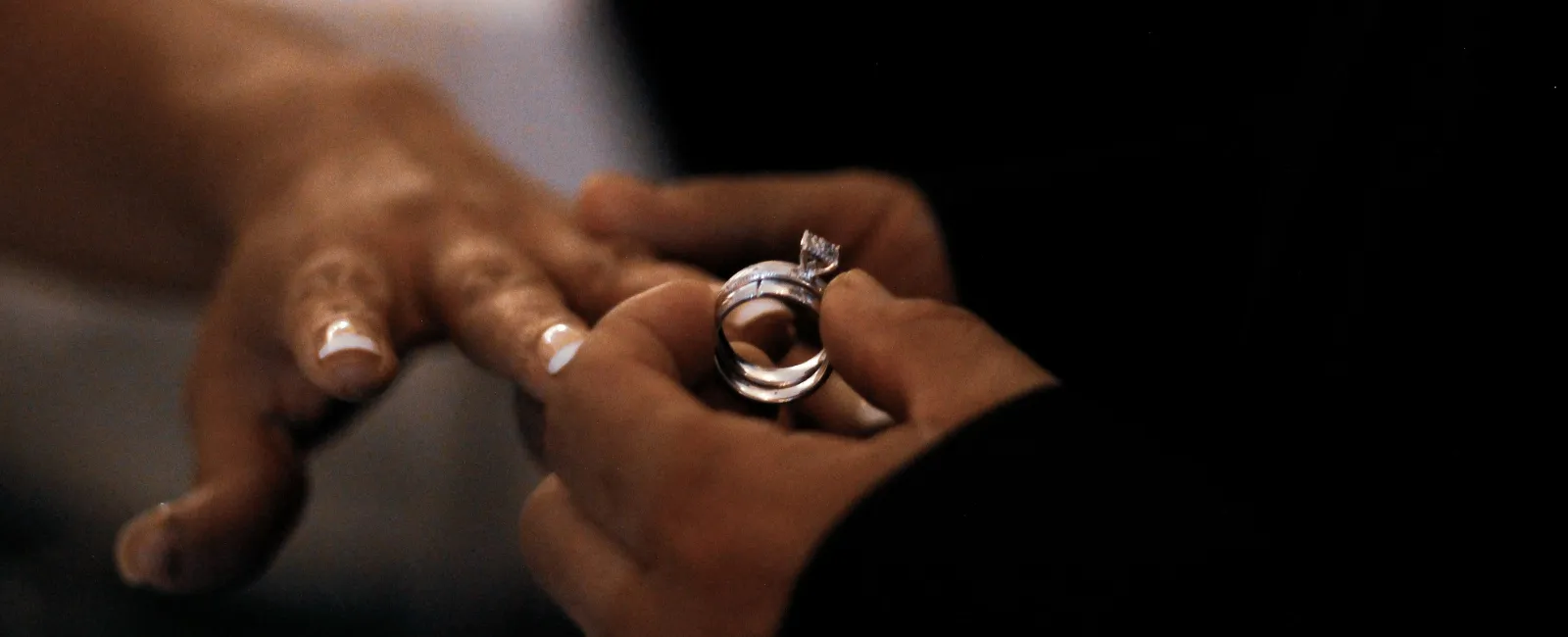 Close-up of a person holding a diamond engagement ring ready to place it on another's finger during a proposal.