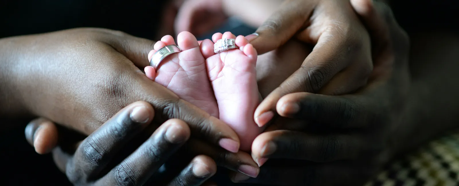 Adult hands gently hold a newborn's feet adorned with two rings symbolizing family and love.
