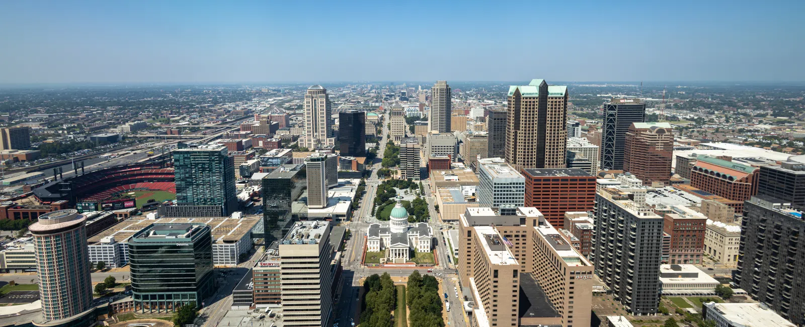 Aerial view of downtown St. Louis showing city skyline, Gateway Arch grounds, and Busch Stadium on a clear day.