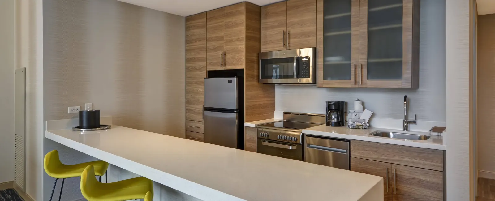 Modern kitchen with wood cabinets, stainless steel appliances, white countertop island, and yellow bar stools.