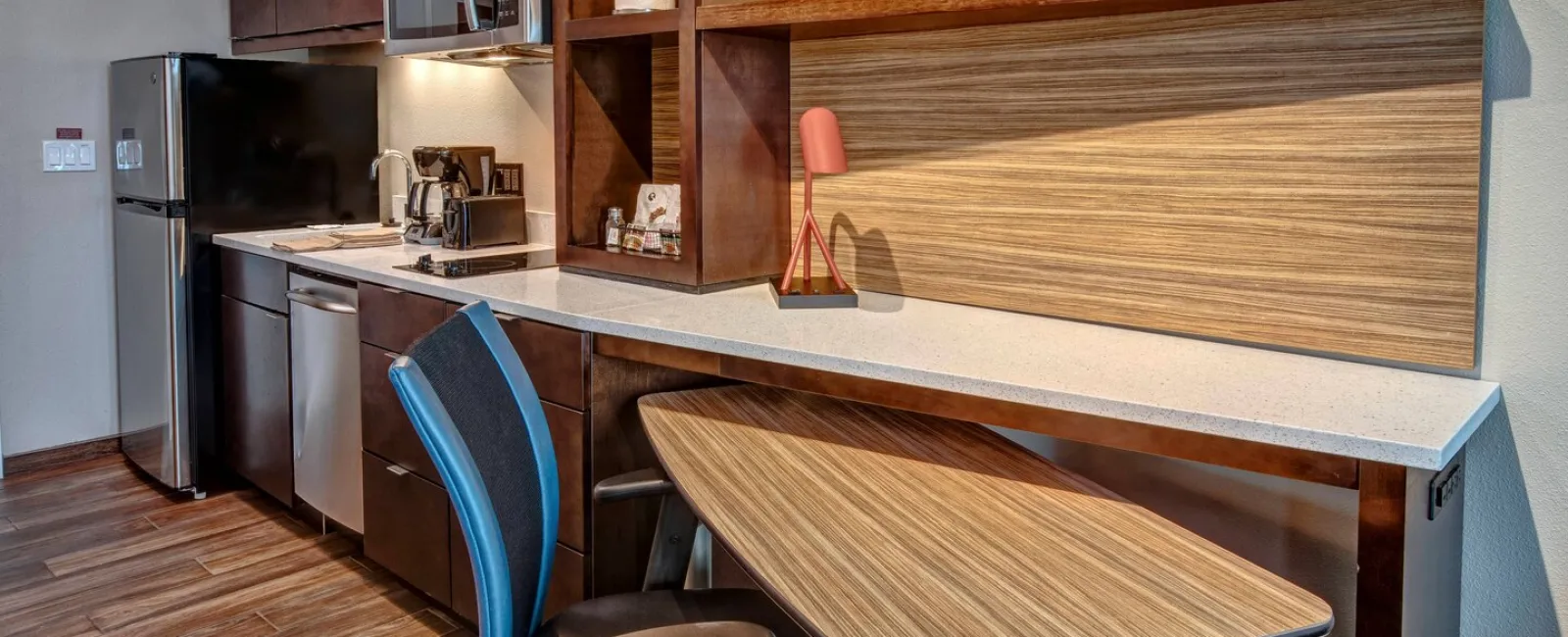 Modern kitchen with stainless steel appliances, wooden cabinets, a built-in desk, and a black office chair.
