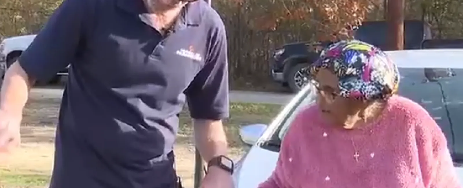 Technician surprising elderly woman with a new HVAC system delivery outdoors near basketball hoop and parked cars