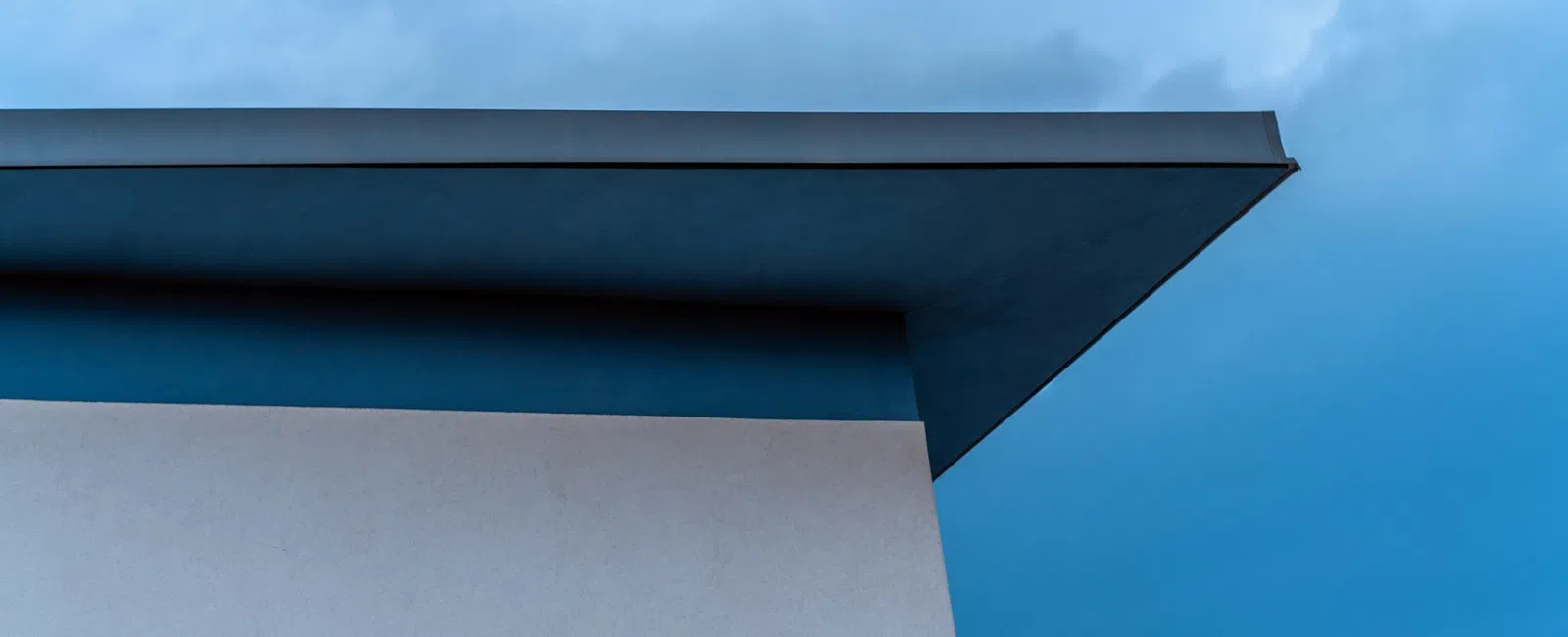 Minimalist building corner with a sharp roof edge against a cloudy blue sky background