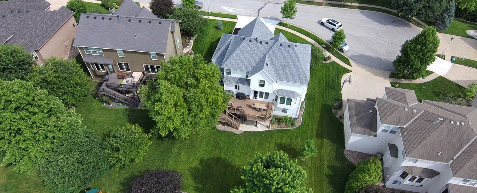 Aerial view of suburban neighborhood with houses, green lawns, trees, playground and curved roads on a sunny day