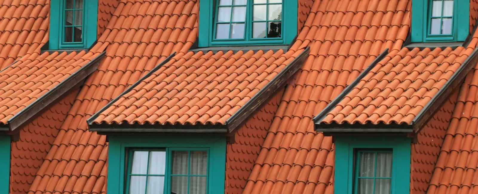 Orange terracotta roof tiles with green-framed windows and dormers on a residential building.