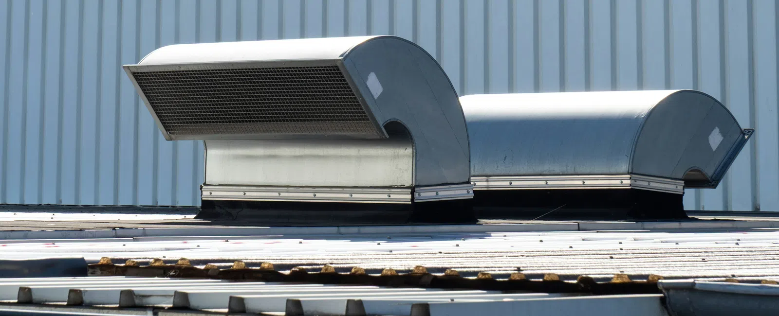 Industrial metal air vents on a corrugated metal rooftop against a striped metal wall background.