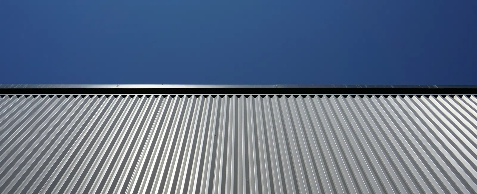 Silver metal building facade with vertical ridges under clear blue sky on a sunny day