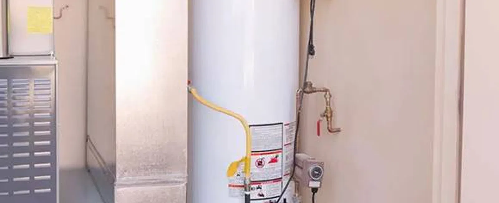 White residential water heater installed next to furnace with pipes and control valves connected