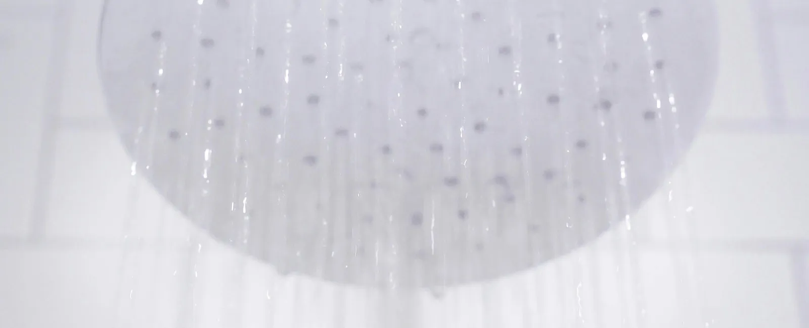 Close-up of a modern showerhead with water cascading down in a bright bathroom.