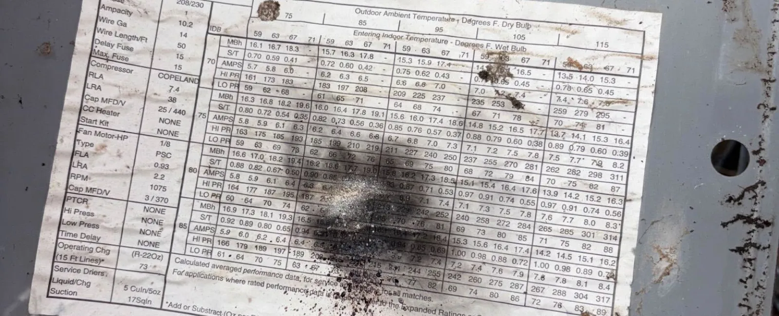 Hand holding a metal panel with a weathered technical specification label outdoors over grass.