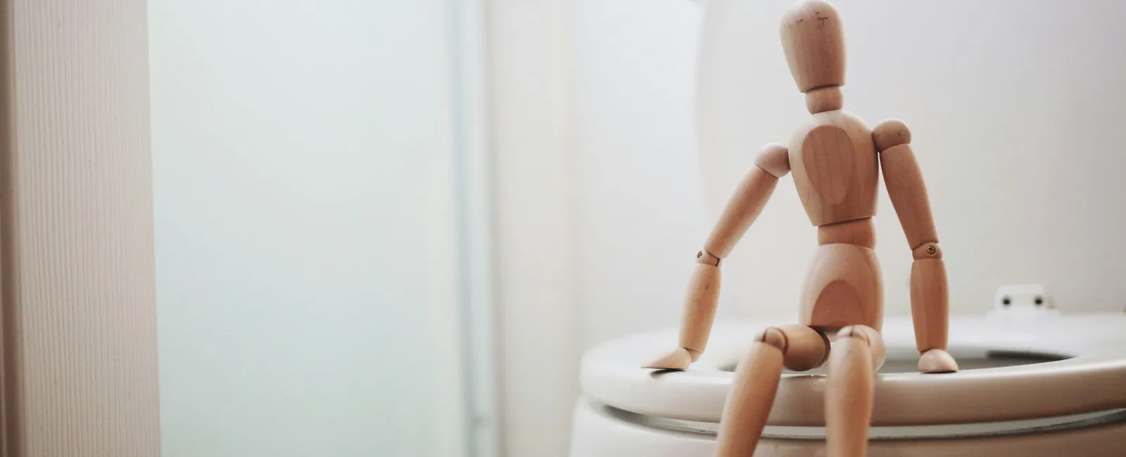 A wooden mannequin sitting on a toilet, illustrating humor in everyday situations.