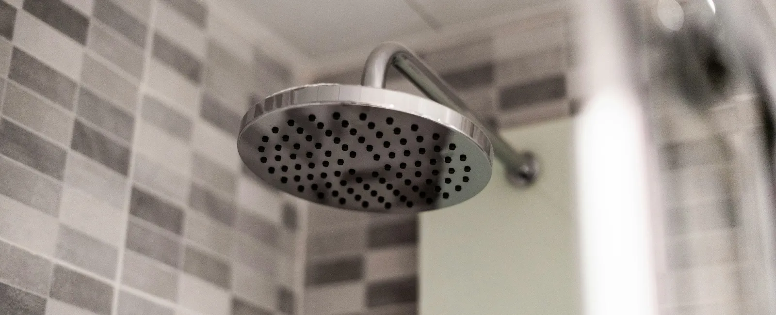 Close-up of a modern round metal showerhead with gray and white tiled wall background in bathroom.