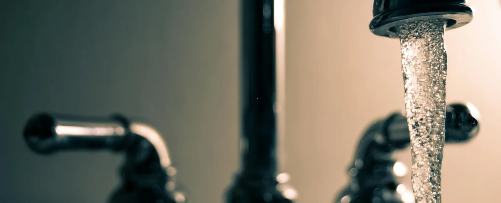 Close-up of a chrome kitchen faucet with water flowing and bubbles forming.