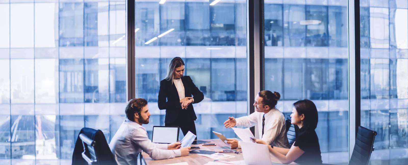Business professionals in formal attire discussing documents around a conference table in a modern office.