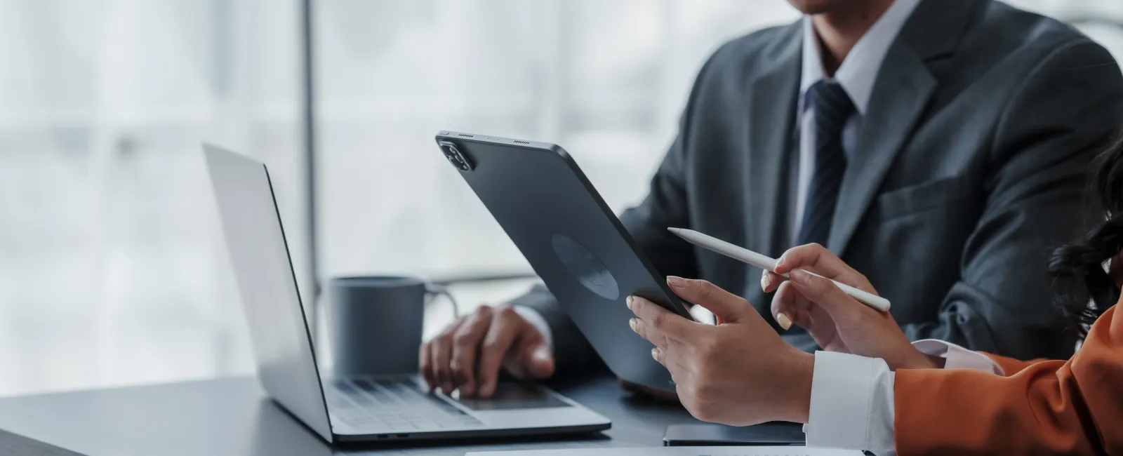 Business professionals collaborating using tablet, laptop, and documents in a modern office setting.