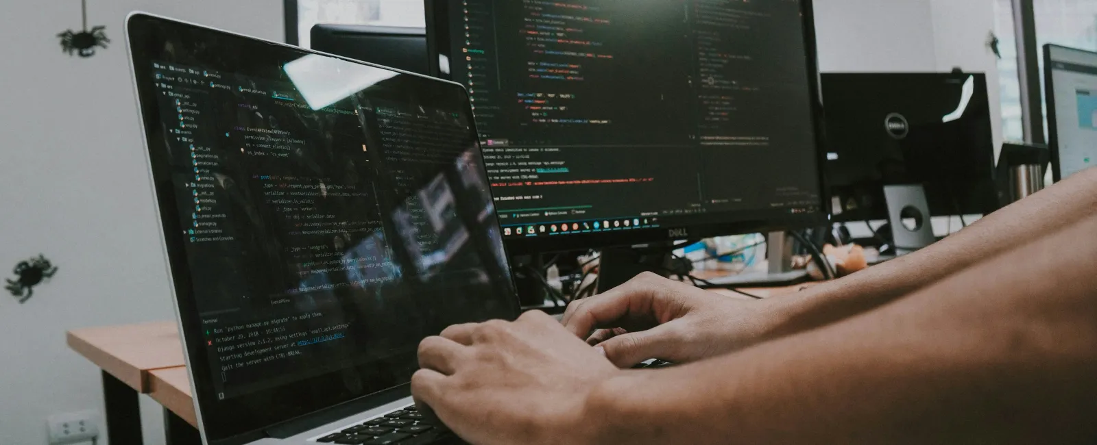 Person coding on laptop with multiple monitors displaying programming code in a modern office environment