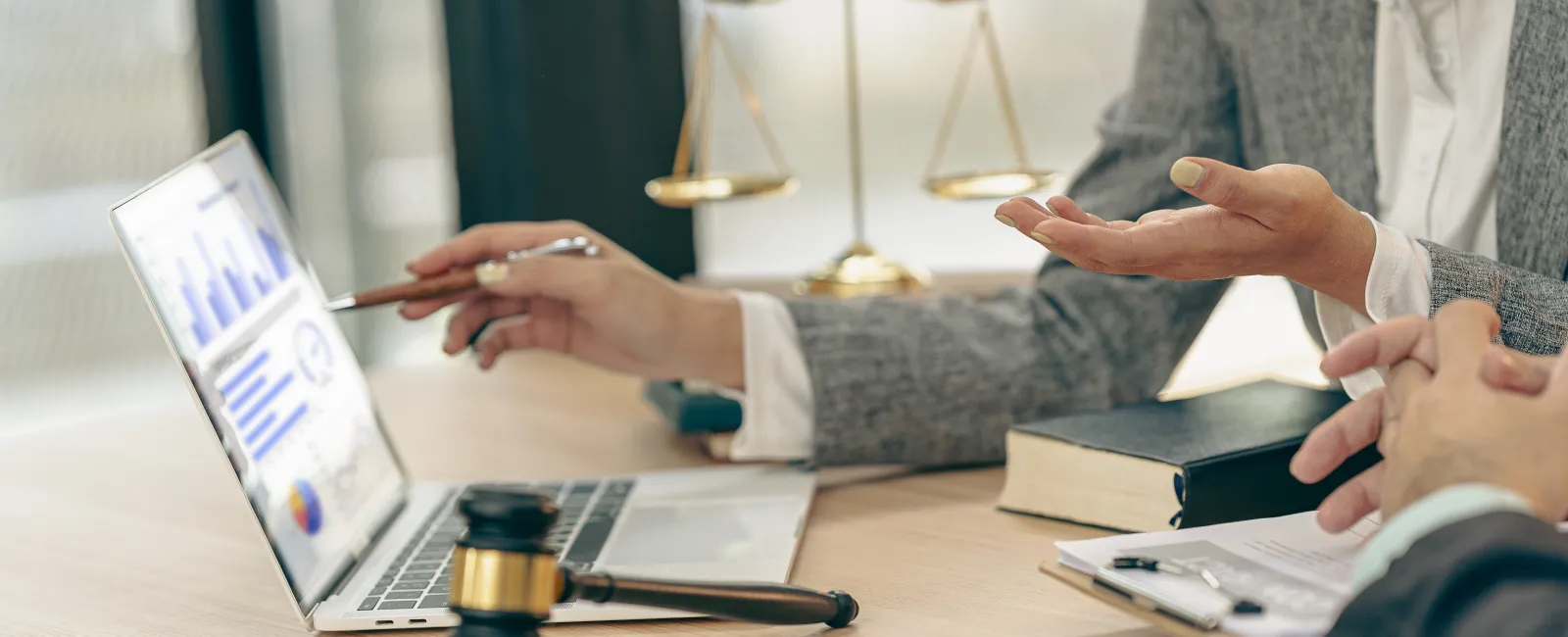 Lawyers discussing data on laptop with legal symbols like gavel and scales on desk in office setting.