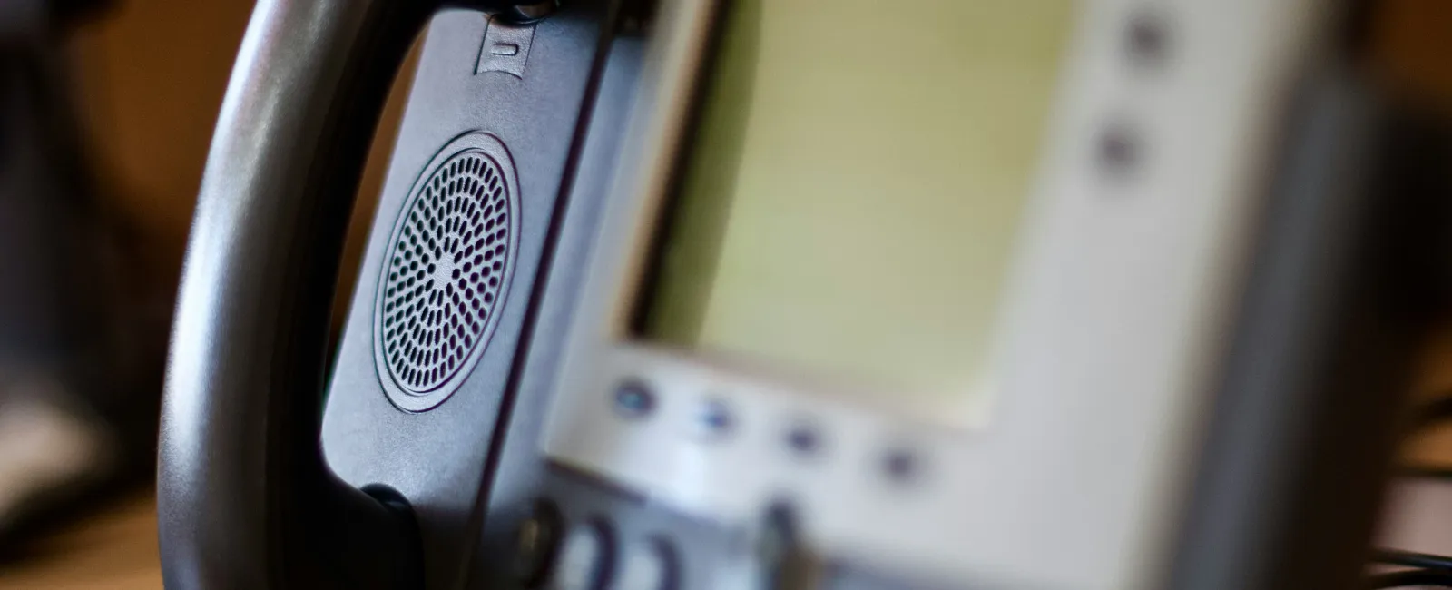 Close-up of a modern business phone handset and blurred digital display with keypad in the background.
