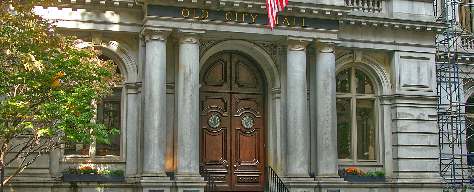 A local Historic Old City Hall building facade with large wooden doors, stone columns, American flag.