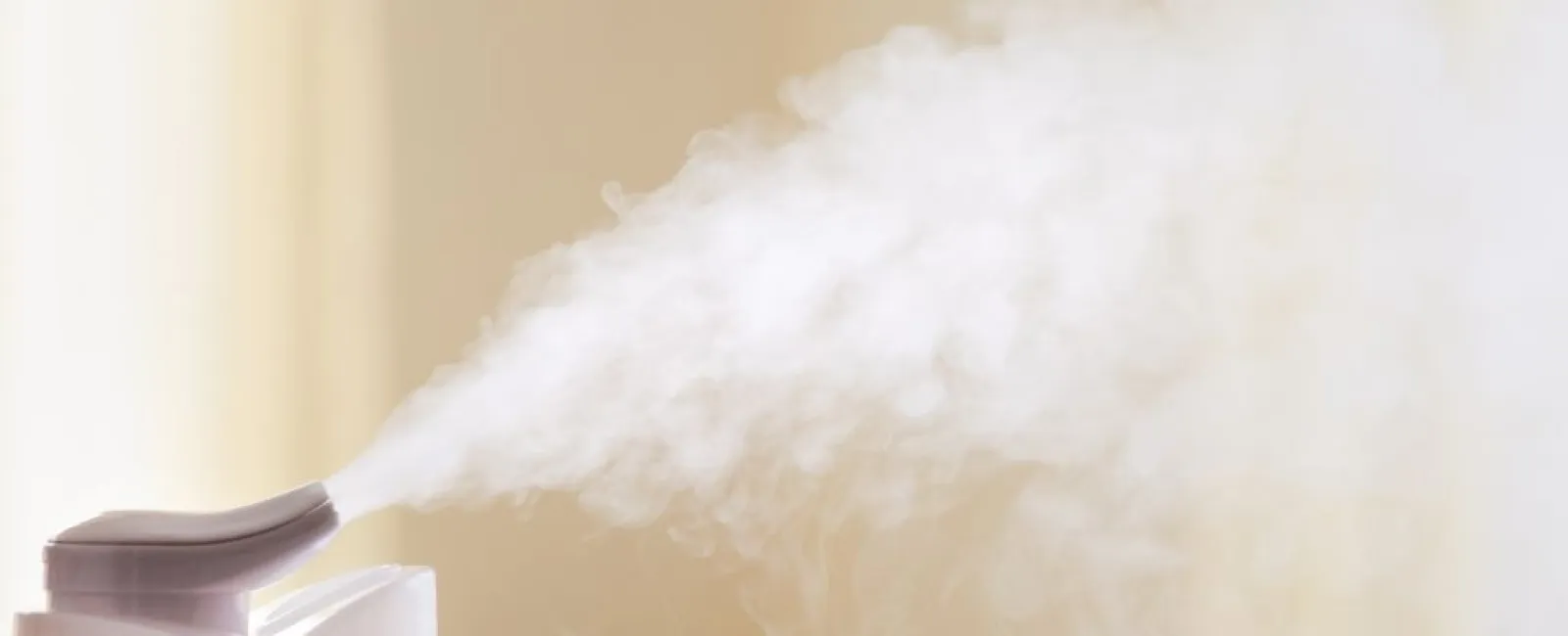 White humidifier releasing mist in a softly lit room with a beige background.
