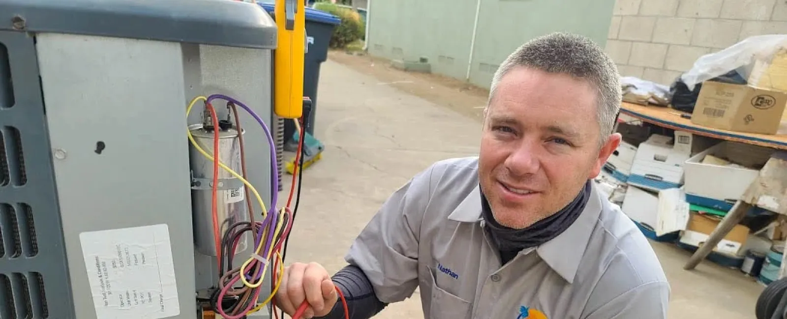Technician wearing a sun hat and mask services a York HVAC unit on a rooftop with tools and hoses connected.